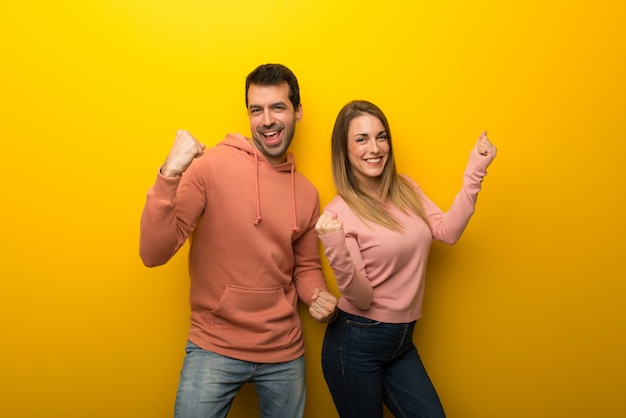 Dos personas sobre fondo amarillo celebrando una victoria.