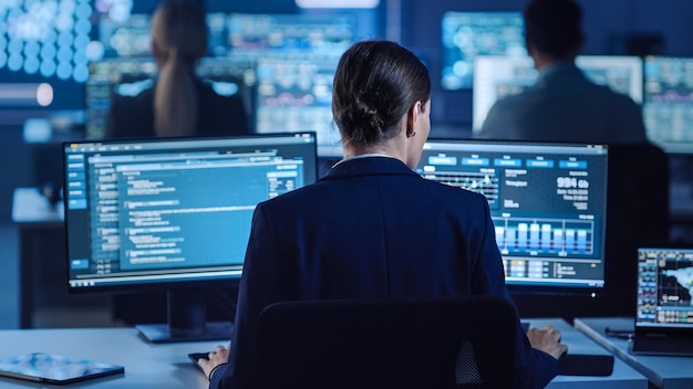 Dos personas trabajando en computadoras en una habitación oscura, una de ellas está mirando una pantalla que dice datos.