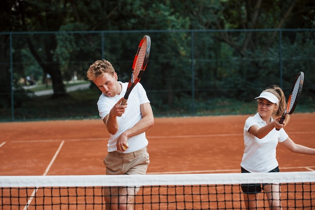 Dos personas en uniforme deportivo juegan al tenis juntos en la cancha.
