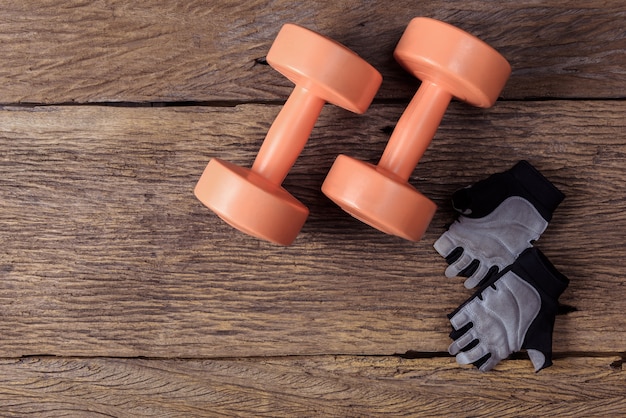 Dos de pesas de gimnasia y guantes protectores en piso de madera en gimnasio, aptitud. Vista superior