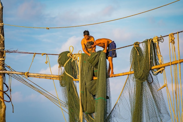 Dos pescadores lanzando redes en cañas de pescar en un hermoso amanecer Los pescadores tradicionales preparan la red de pesca que la gente local llama Day hang khoi Concepto de pesca y vida cotidiana