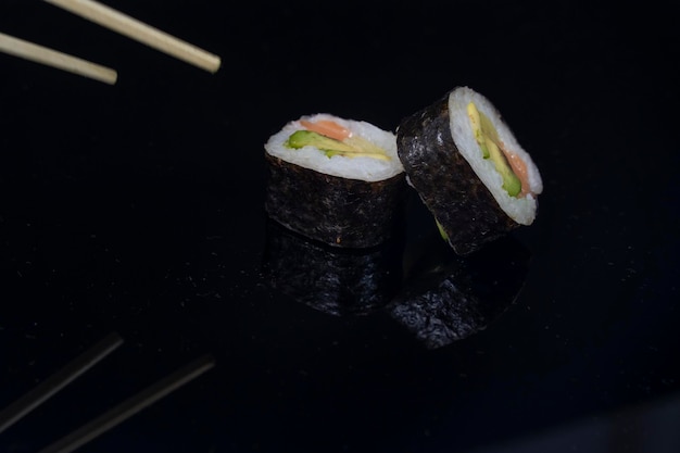 Dos piezas de sushi con palillos en fondo oscuro