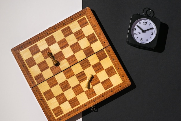 Dos piezas, un tablero de ajedrez y un reloj sobre un fondo blanco y negro.