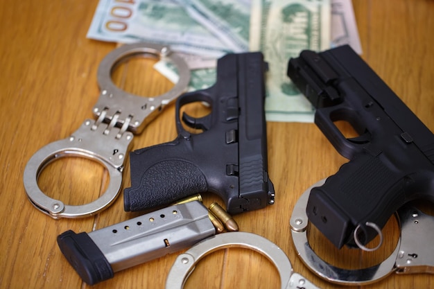 Foto dos pistolas semiautomáticas con esposas proyectiles de 9 mm y billetes de dólares estadounidenses en un fondo borroso pistola pistola dos esposas de policía y billetes de dólares estadounidenses dinero en una mesa de madera