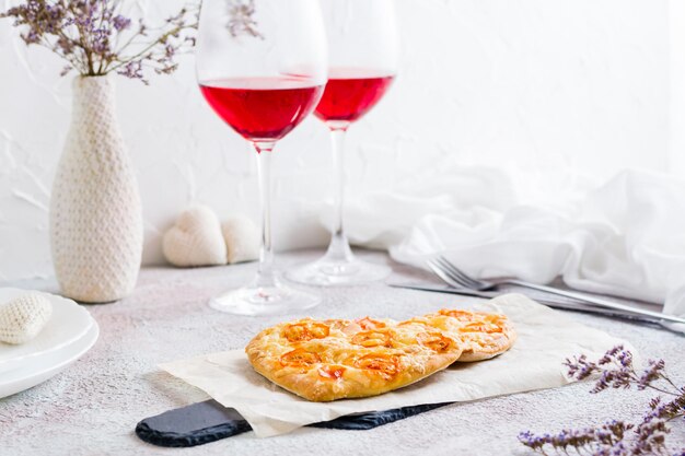 Dos pizzas en papel en forma de corazón y dos copas de vino en una mesa para la celebración del día de san valentín