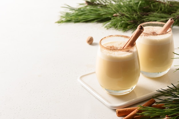 Dos ponche de huevo de Navidad con canela rallada y nuez moscada sobre fondo blanco.