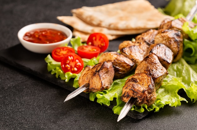 Dos porciones de shish kebab en una placa de piedra con ensalada.