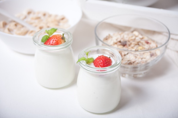 Dos porciones de yogurt natural casero en un frasco de vidrio con fresas frescas y muesli cerca