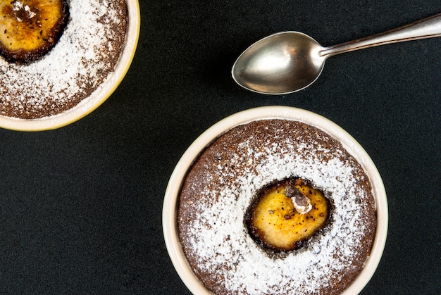 Dos postres de chocolate con una pera en una mesa de piedra negra, vista superior