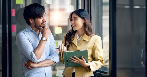 Dos profesionales creativos discutiendo la estrategia de planificación de interrupción del mercado de aumento de ingresos de pie cerca de la ventana en la oficina