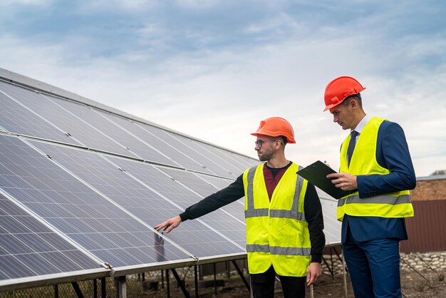 Dos profesionales de la ropa de trabajo hablan sobre los paneles solares y su impacto. El concepto de electricidad verde y su impacto