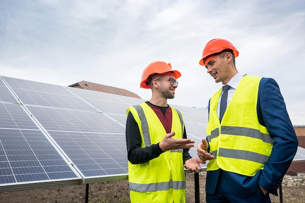 Dos profesionales trabajadores en cascos y chalecos discuten el proceso de trabajo de instalación de paneles El concepto de instalación de paneles solares