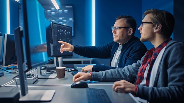 Dos programadores profesionales de TI discutiendo el diseño y desarrollo de la arquitectura de la red de datos Blockchain mostrado en la pantalla de la computadora de escritorio Departamento técnico de centro de datos de trabajo con bastidores de servidores