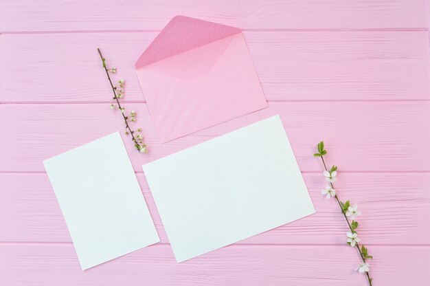 Dos ramas de flores de cerezo blanco sobre fondo de madera rosa con hoja de papel