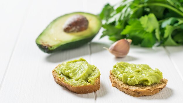 Dos rebanadas de pan con guacamole y aguacate sobre una mesa blanca. Dieta vegetariana comida mexicana aguacate. Alimentos crudos.