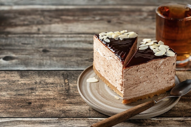 Dos rebanadas de pastel de queso de chocolate glaseado con cobertura de pétalos de almendras y taza de té sobre fondo de madera con espacio de texto