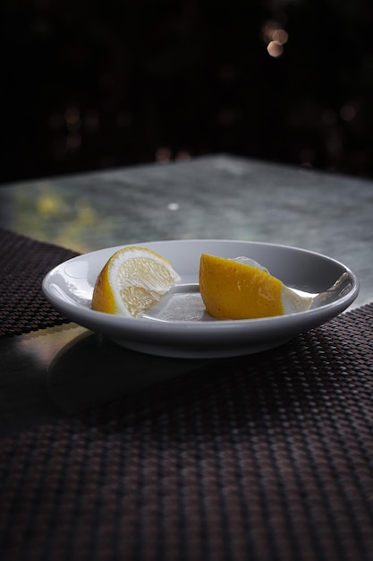 Dos rodajas de limón se encuentran en un plato blanco. Limón sobre un fondo oscuro.