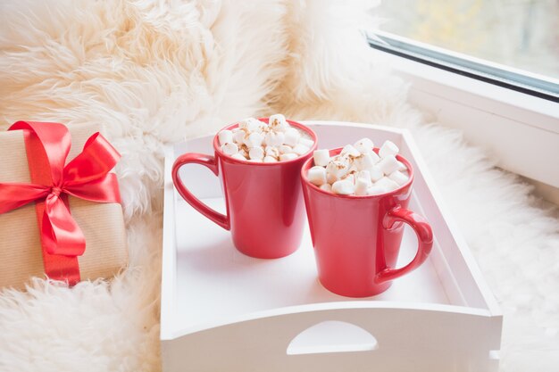 Dos rojo taza de chocolate caliente con malvavisco en el alféizar de la ventana