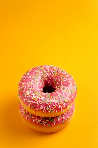 Dos rosquillas rosadas en la pared amarilla vista superior copia espacio