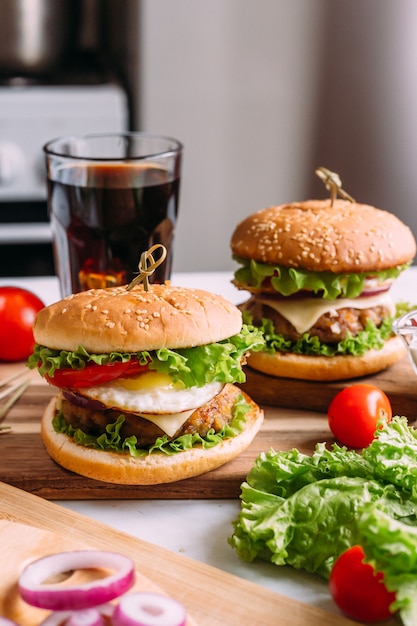 Dos sabrosas hamburguesas caseras con lechuga y queso. Ingredientes en la mesa. Fondo de comida ligera.