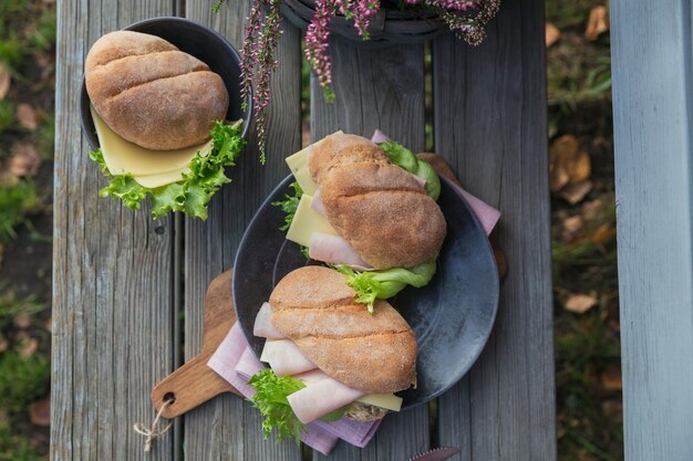 Dos sándwiches de baguette ciabatta frescos con jamón, queso y lechuga sobre fondo de madera rústica