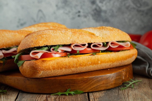 Dos sándwiches de baguette largo con rebanadas de rúcula de tomate fresco, jamón y queso.