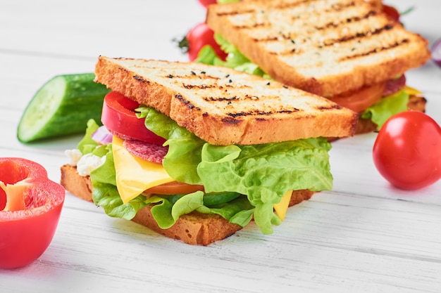 Dos sándwiches con jamón, lechuga y verduras frescas sobre un fondo blanco.
