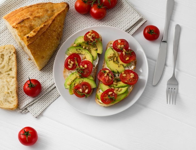 Dos sándwiches o tapas preparados con diferentes verduras, como aguacate, tomate y tomillo fresco con piñones.