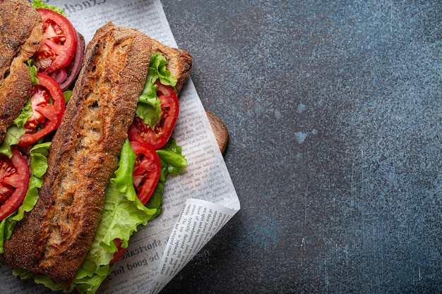 Dos sándwiches de pan ciabatta oscuro con ensalada verde tomates rojos maduros cebolla y atún