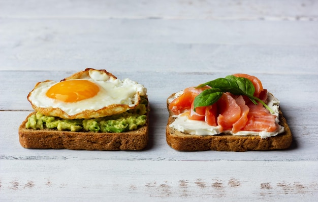 Dos sándwiches con queso crema de salmón ahumado, aguacate y huevo frito Concepto para un desayuno saludable