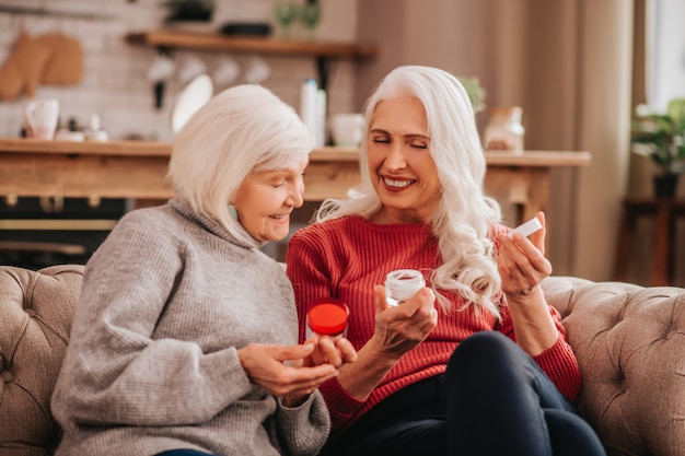 Dos señoras lindas agradables canas discutiendo nuevos cosméticos