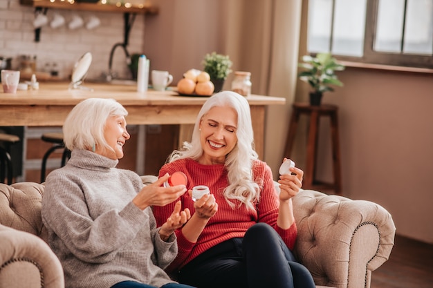 Dos señoras lindas agradables de pelo gris hablando de nuevas cremas anti-envejecimiento