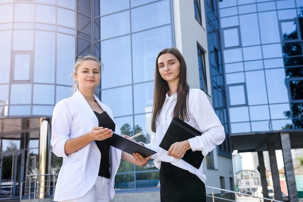 Dos señoras de negocios jóvenes posando fuera del edificio de oficinas. Mujer y empresa