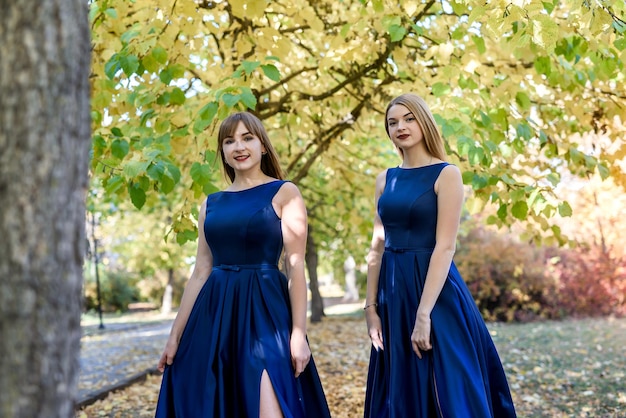 Dos señoritas muy hermosas en vestidos azules de moda en el parque de otoño.