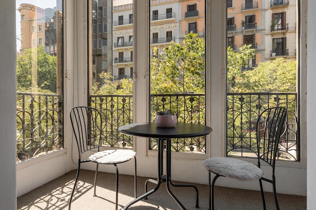 Dos sillas de hierro y mesa en terraza acristalada cerrada con hermosa vista de nueva y acogedora zona de cálido