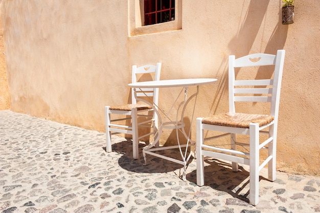 Dos sillas de madera blanca con mesa en la calle. Arquitectura griega tradicional en la isla de Santorini, Grecia.