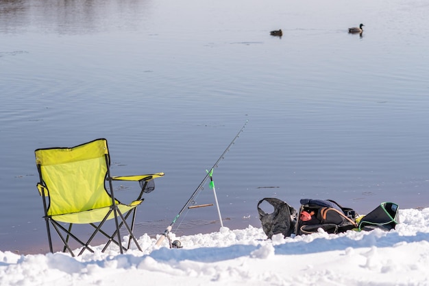 Dos sillas en la nieve con una caña de pescar y una bolsa de aparejos de pesca.