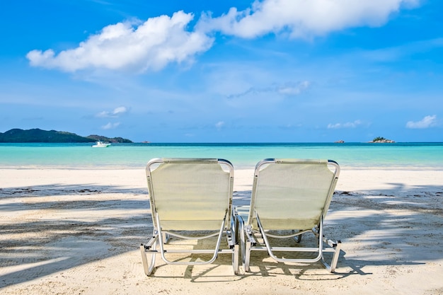 Dos sillas de playa blanca en la playa de arena tropical, espacio de copia