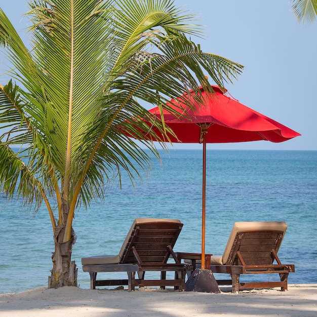 Dos sillas de playa, sombrilla roja y palmera en la playa de Tailandia