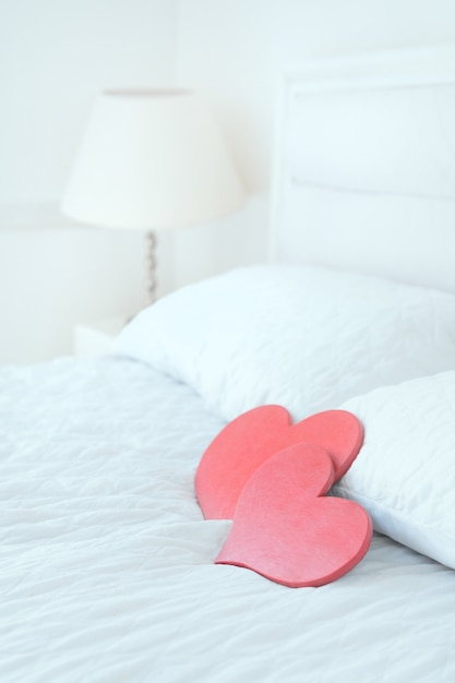 Dos símbolos rojos del corazón en la cama blanca. Interior limpio blanco con corazones rojos de madera. Concepto de dia de san valentin