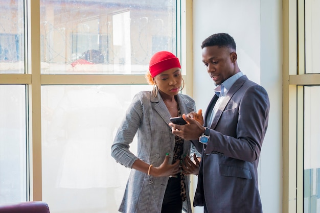 Dos socios de negocios africanos jóvenes discutiendo sobre lo que vieron en su teléfono celular.