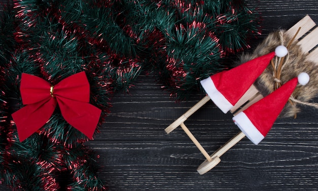 Dos sombreros de Santa en un juguete trineo de Navidad, lazo de Navidad y oropel verde y rojo sobre negro