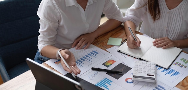 Dos sonrientes empresarias asiáticas de mediana edad discutiendo y trabajando con una tableta en la oficina