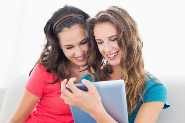 Dos sonrientes jóvenes amigas usando tableta digital