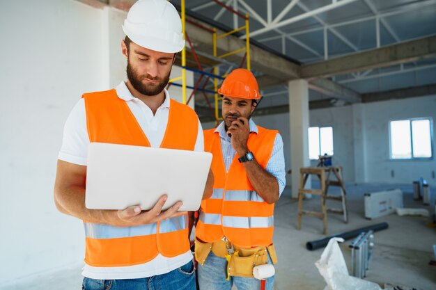 Dos supervisores especialistas en cascos con laptop en el sitio de construcción para trabajar