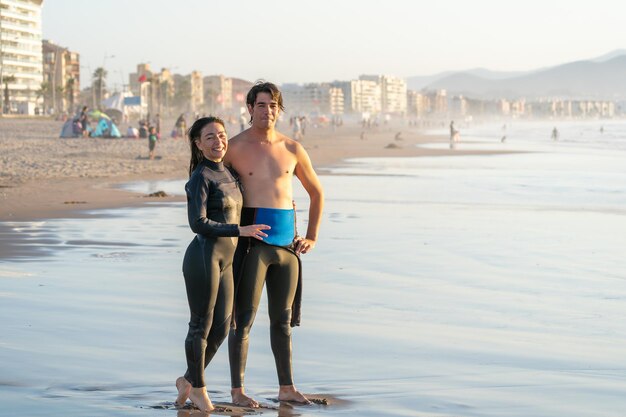 Dos surfistas latinos en la playa abrazándose y sonriendo