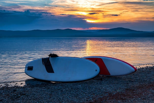 Dos tablas de sopa en la orilla de un pintoresco lago contra el telón de fondo de la puesta de sol