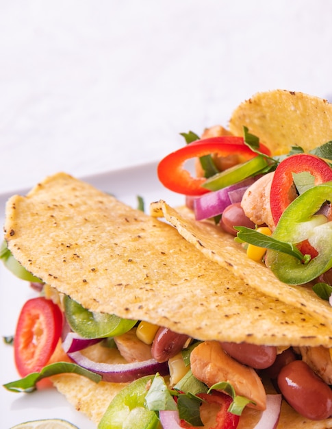 Dos tacos mexicanos con pollo, cebolla, chiles, maíz y frijoles en un plato para servir sobre fondo blanco. Macro y vista cercana