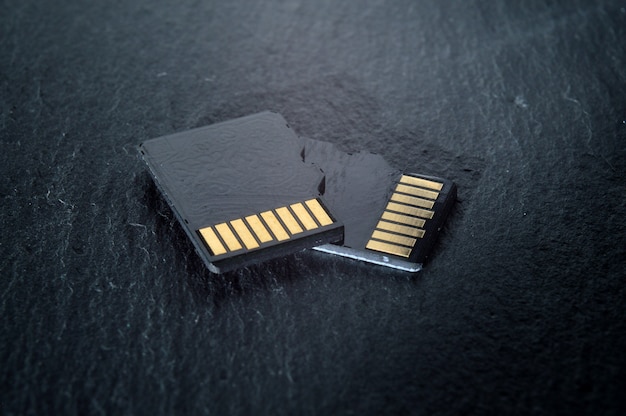 Dos tarjetas micro sd se encuentran una encima de la otra sobre un fondo de textura oscura, con contactos dorados en la parte superior. de cerca.