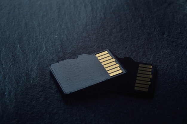 dos tarjetas micro sd se encuentran una encima de la otra sobre un fondo de textura oscura, con contactos dorados en la parte superior. de cerca.